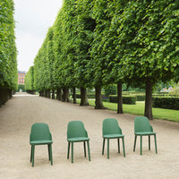 Four sleek, green chairs arranged in a row on a gravel path, surrounded by lush greenery and symmetry.