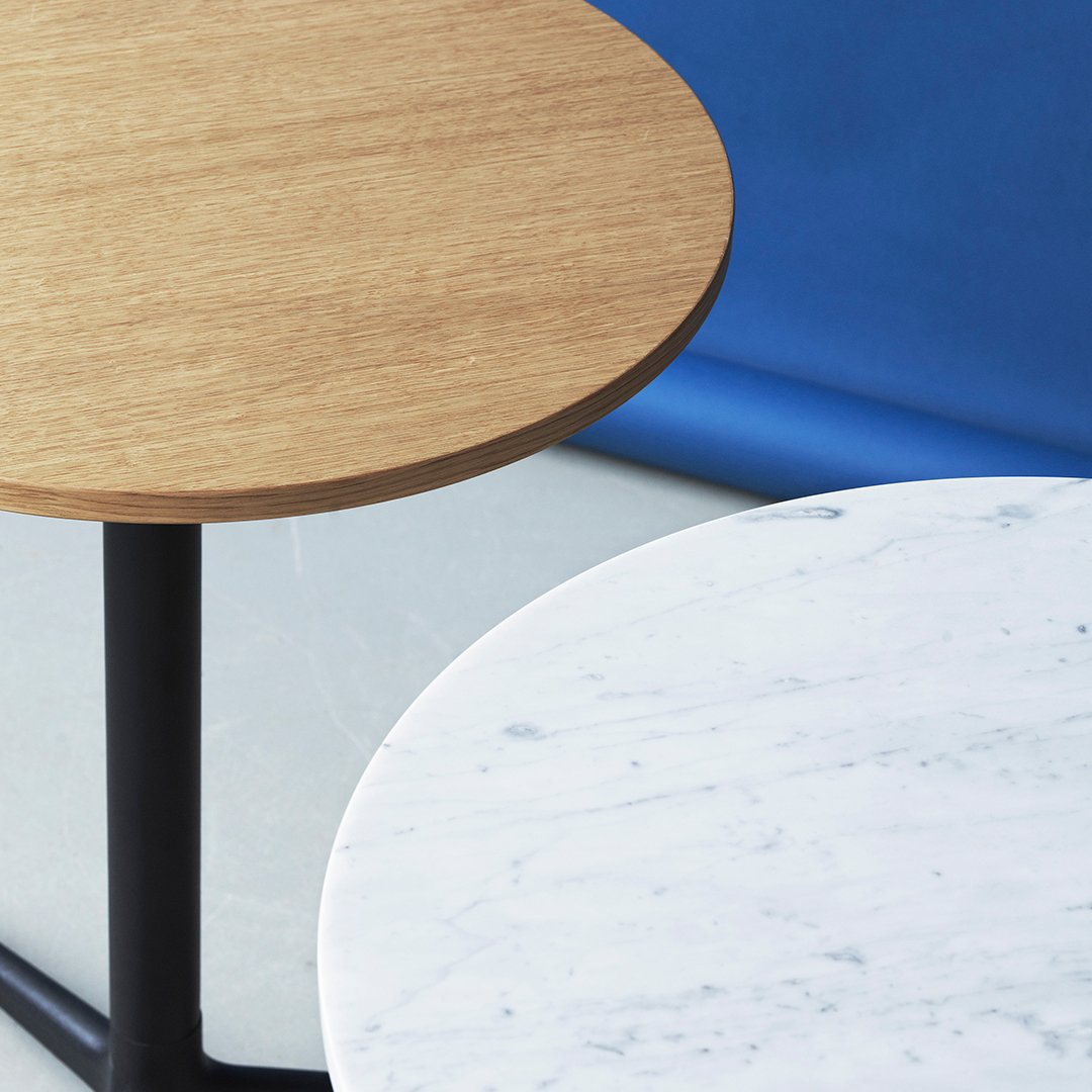 Wooden tabletop in natural oak finish and round white marble top with subtle gray veining against a blue backdrop.