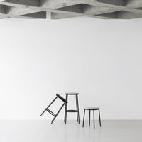 Minimalist black bar stools with clean lines against a plain white wall and textured gray ceiling.