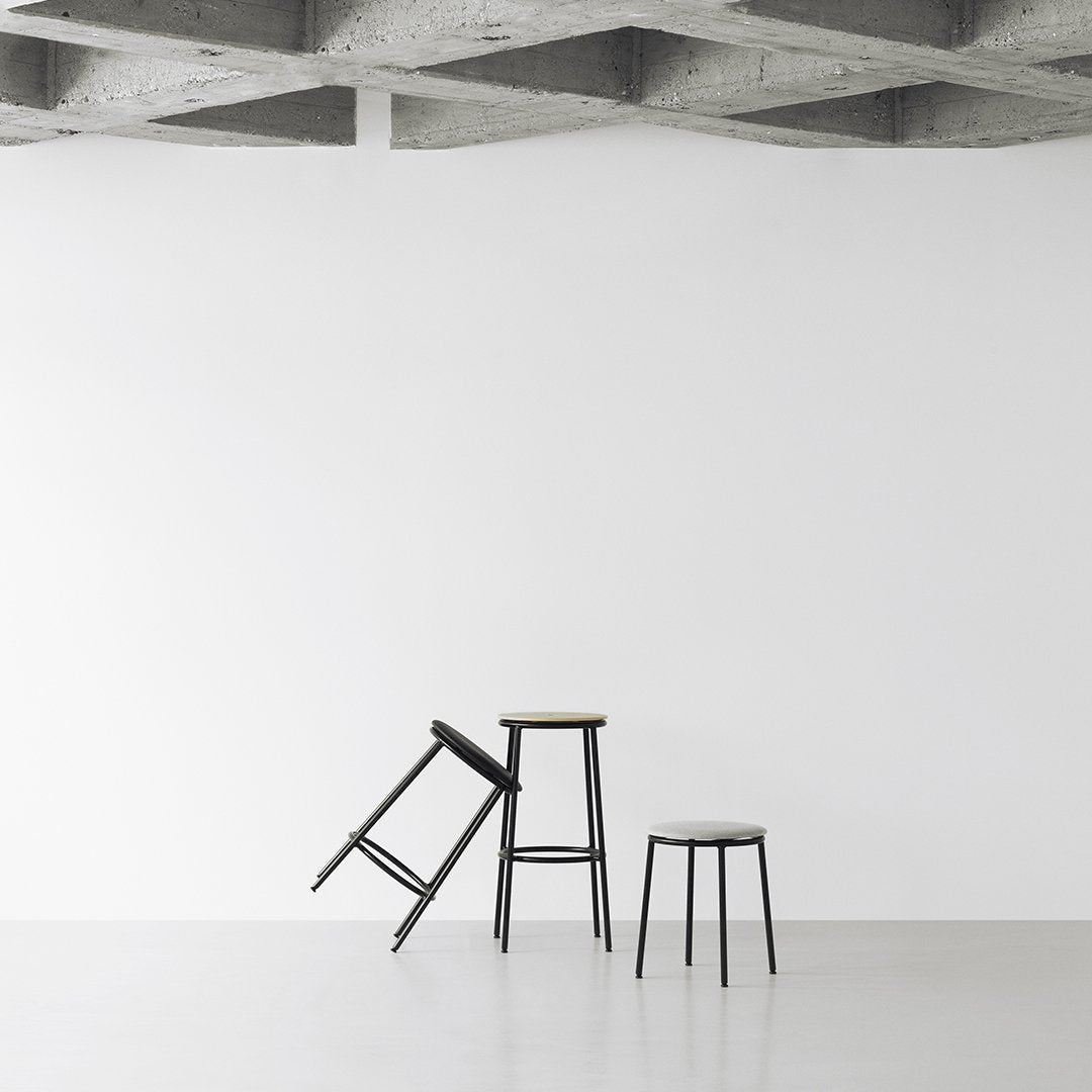 Black metal stools with minimalist design, featuring natural wood accents against a white backdrop and concrete ceiling.