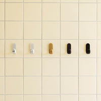 Colorful wall hooks in silver, gold, black, and bronze set against a pale yellow tiled background.