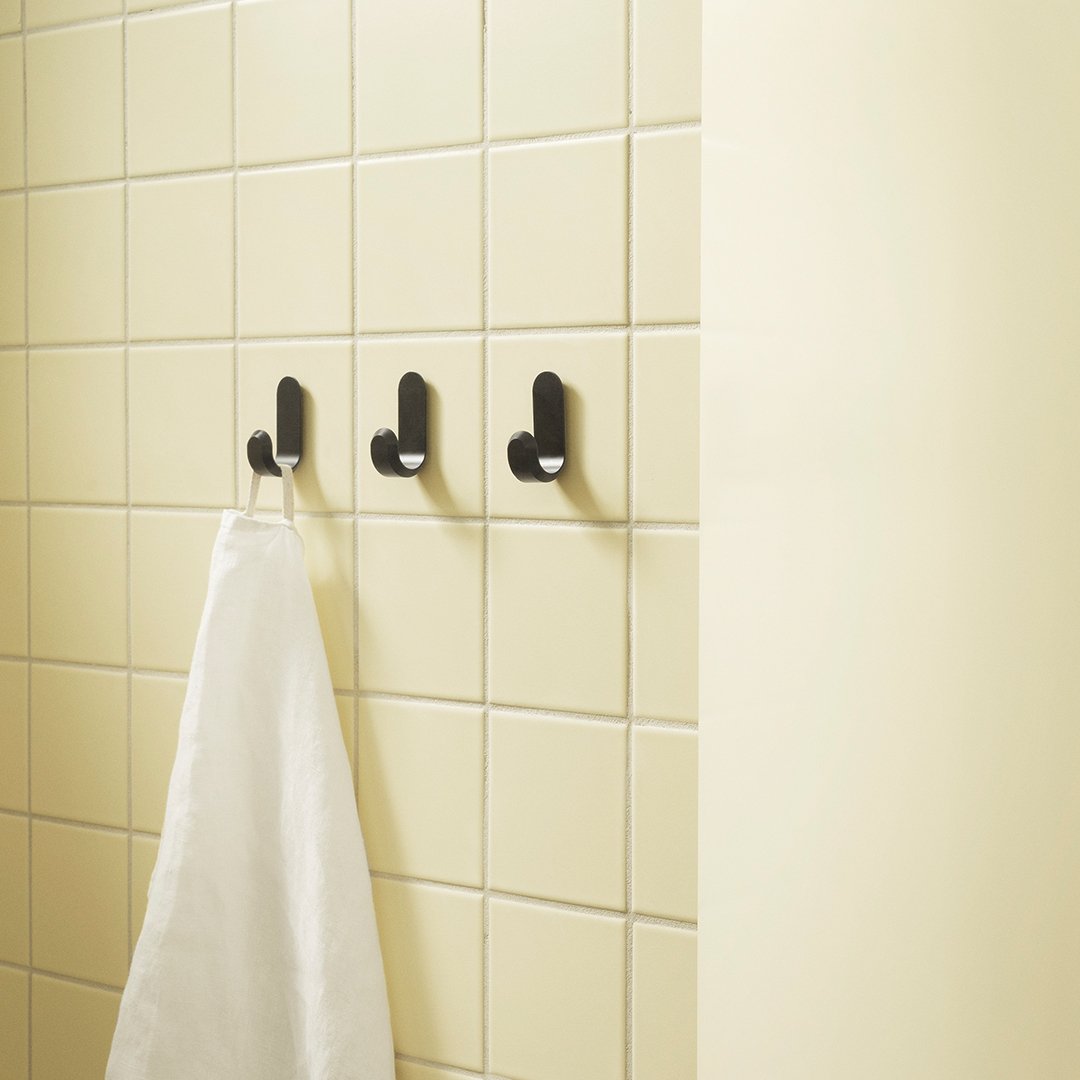 Black wall hooks on a light yellow tiled background with a white towel hanging.