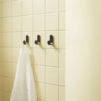 Black wall hooks on a light yellow tiled background with a white towel hanging.