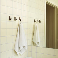 Neutral yellow tiled wall with grid pattern, featuring dark bronze hooks and a white towel hanging.