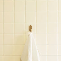 White towel hanging on a light yellow tiled wall with a grid pattern. Soft and minimalist aesthetic.