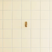 Creamy yellow tiled wall with subtle grid pattern and a small, sleek brown hook.