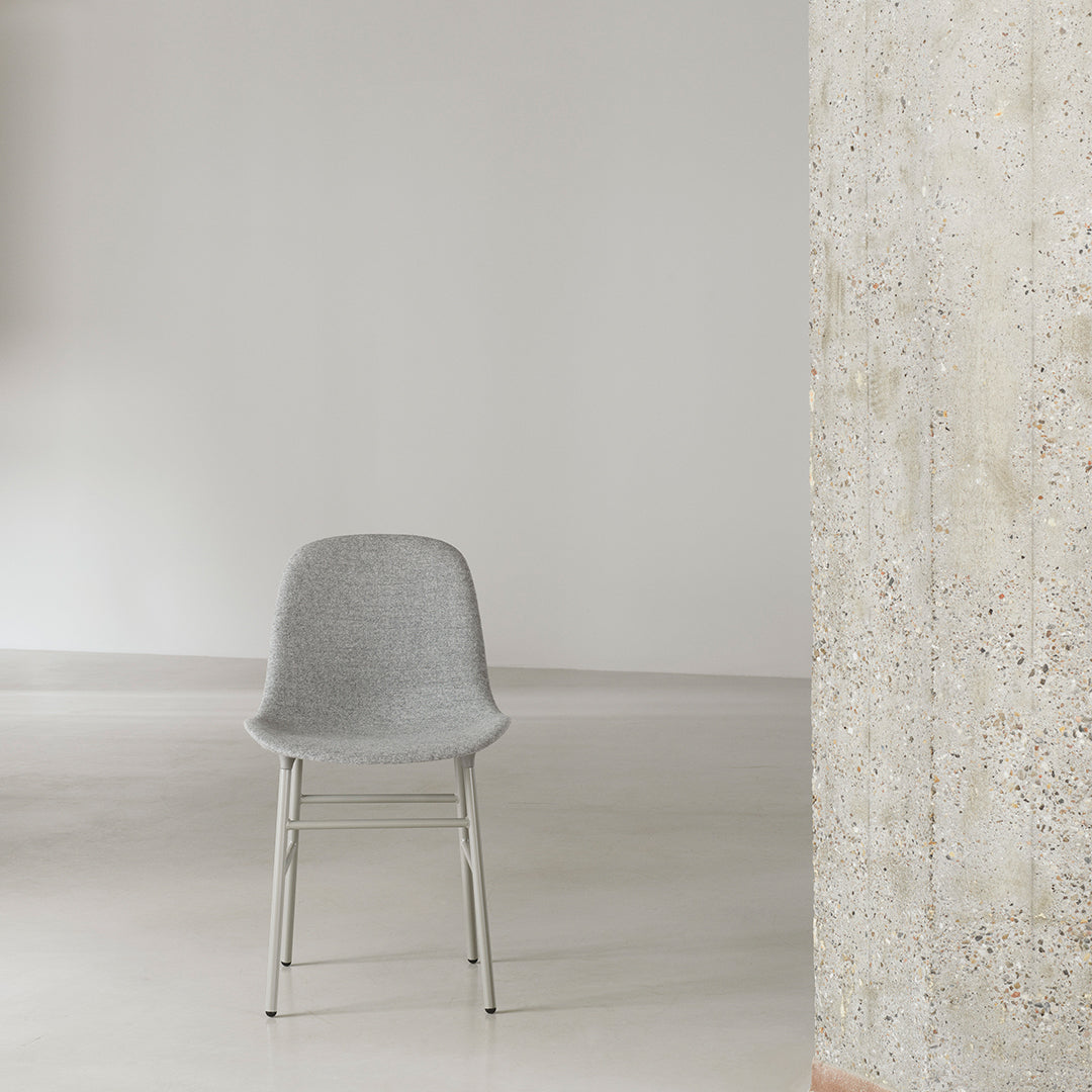 Gray textured chair with sleek metal legs against a minimalist background featuring concrete and smooth floors.
