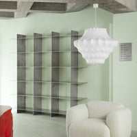 Modern gray shelving unit against a soft green wall, featuring a textured white pendant lamp and a cozy cream armchair.