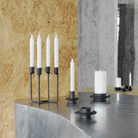 Black and white candle holders with sleek designs, set against warm wood and cool gray surfaces.