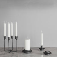 Black candle holders with white candles on a gray background, featuring minimalist design and elegant simplicity.