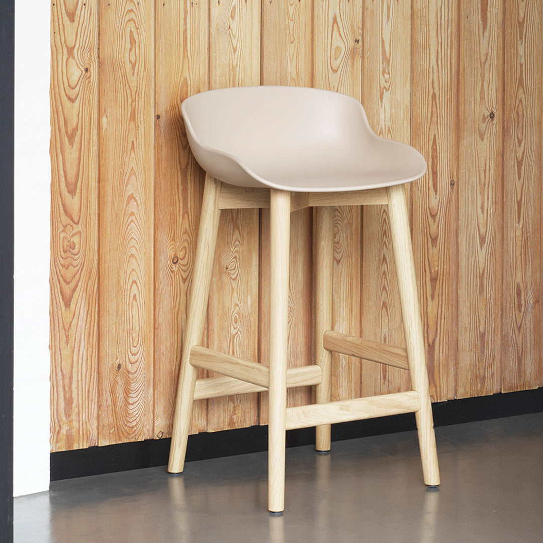 Light beige modern bar stool with natural wood legs against a wooden wall backdrop. Stylish and minimalist design.