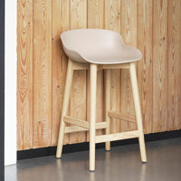 Light beige modern bar stool with natural wood legs against a wooden wall backdrop. Stylish and minimalist design.