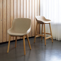 "Beige upholstered chair and bar stool with natural wooden legs against a minimalist backdrop."