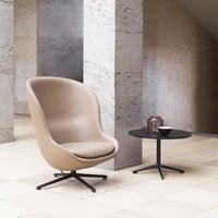 Beige ergonomic chair with a smooth finish, paired with a sleek black side table against a minimalist stone backdrop.