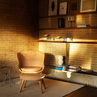 "Light brown curved chair with wooden legs against a textured brick wall and minimalist decor."