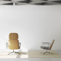Two modern chairs in soft wood and gray upholstery, against a minimalist white background with subtle geometric floor pattern.
