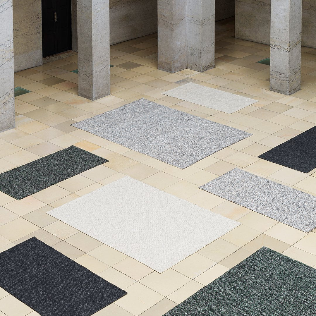 "Textured area rugs in grey, white, dark green, and black patterns on a tiled floor."