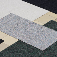 Multicolored textured rug featuring gray, white, green, and black patterns against a tiled backdrop.