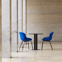 Two vibrant blue chairs beside a sleek black table, set against a textured stone wall.