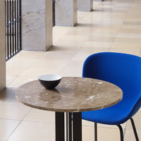 Round marble table with earthy beige tones, paired with a vibrant blue chair and a simple black and white bowl.