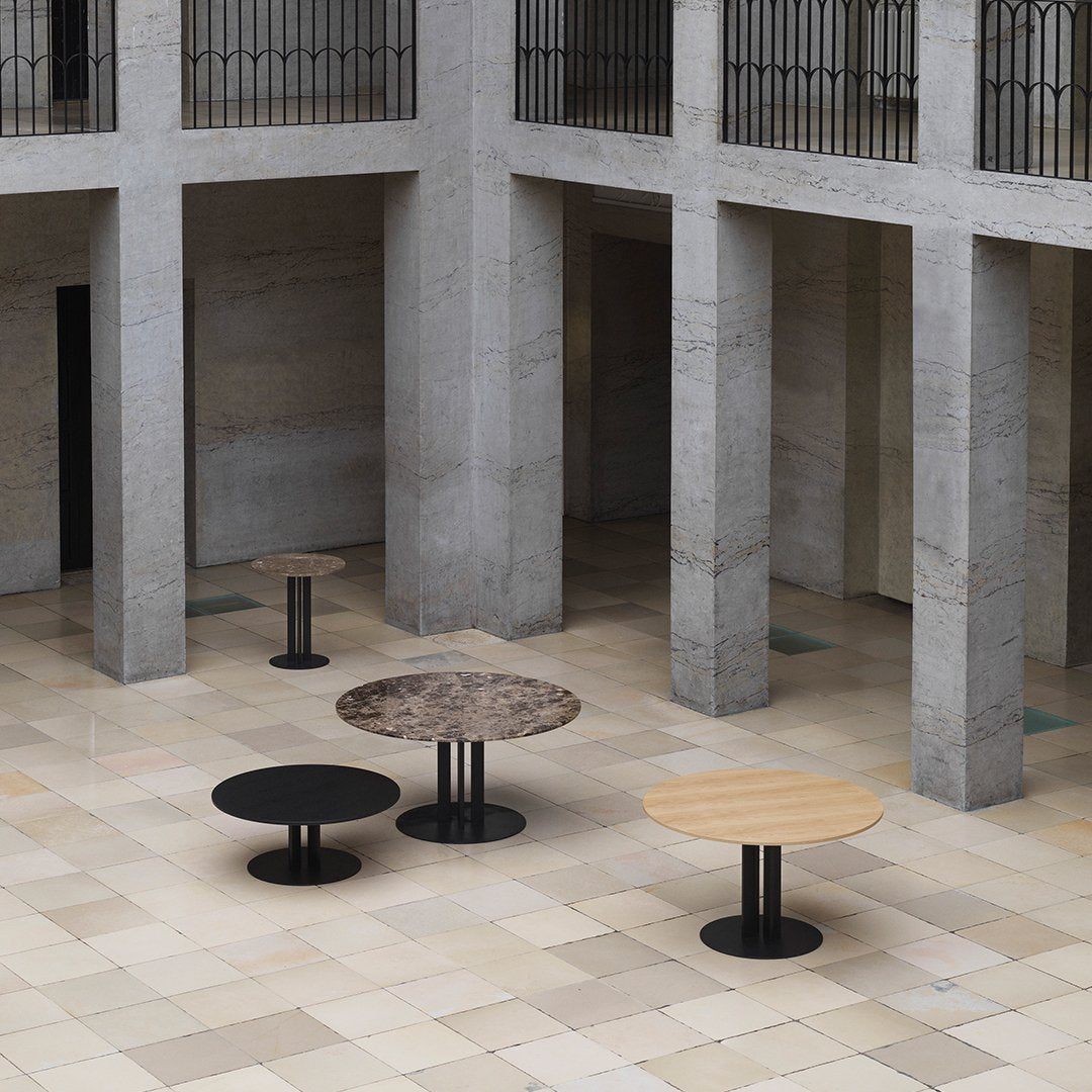 Modern round tables in black, brown marble, and light wood finishes, displayed in a minimalist architectural space.