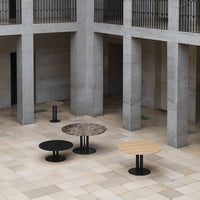 Modern round tables in black, brown marble, and light wood finishes, displayed in a minimalist architectural space.