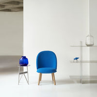 Vibrant blue chair with smooth curves, paired with a deep blue vase and sleek glass shelf, against a minimalistic backdrop.