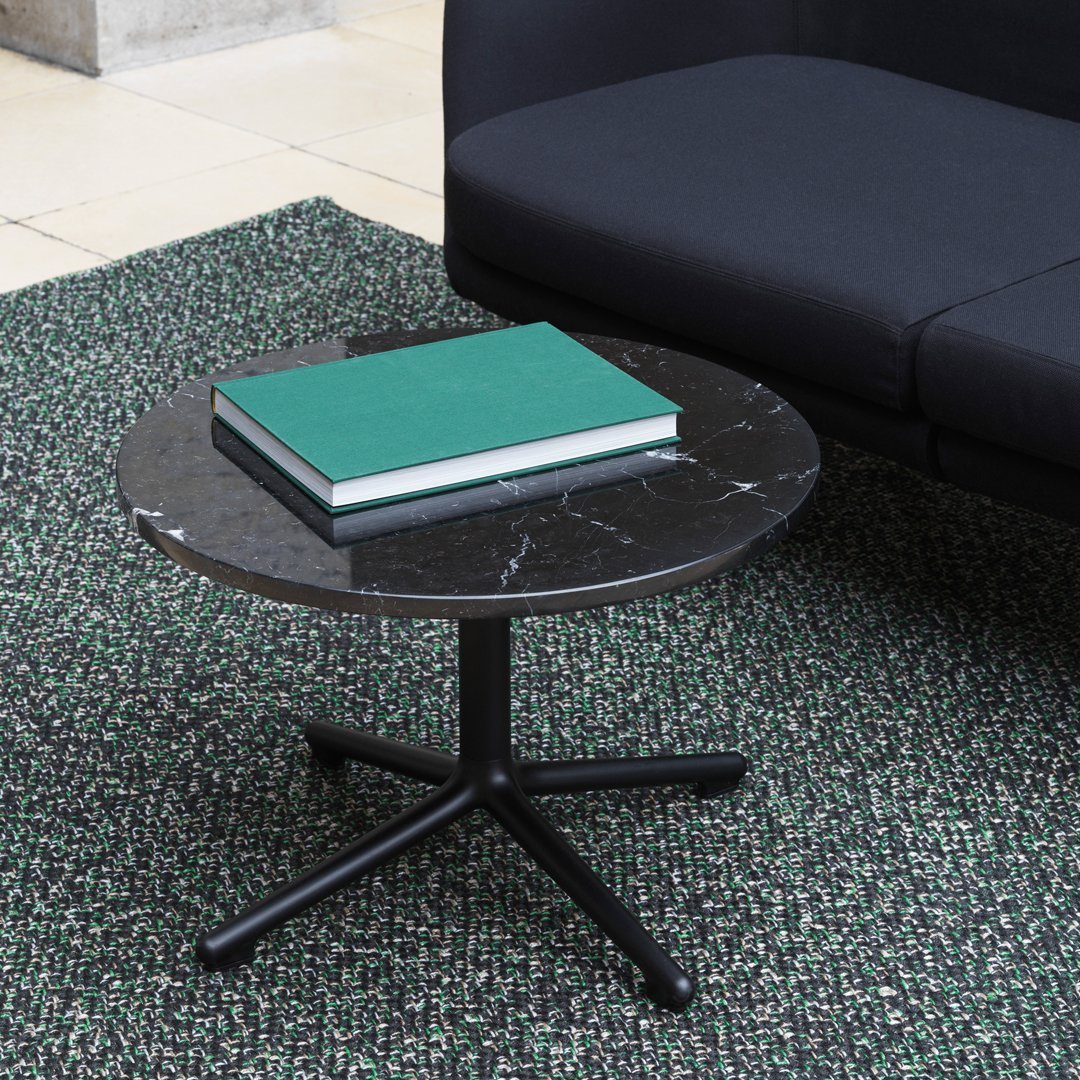 Black marble round coffee table with white veining, set on a modern black base, against a textured green rug.