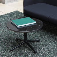 Black marble round coffee table with white veining, set on a modern black base, against a textured green rug.