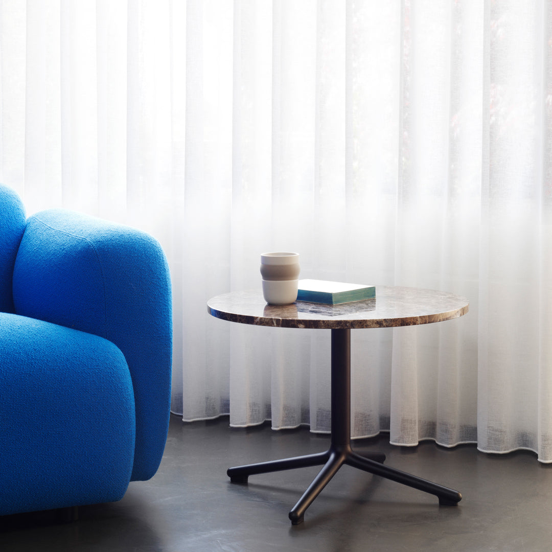 "Round marble coffee table with a dark base, paired with a vibrant blue sofa, against sheer white curtains."