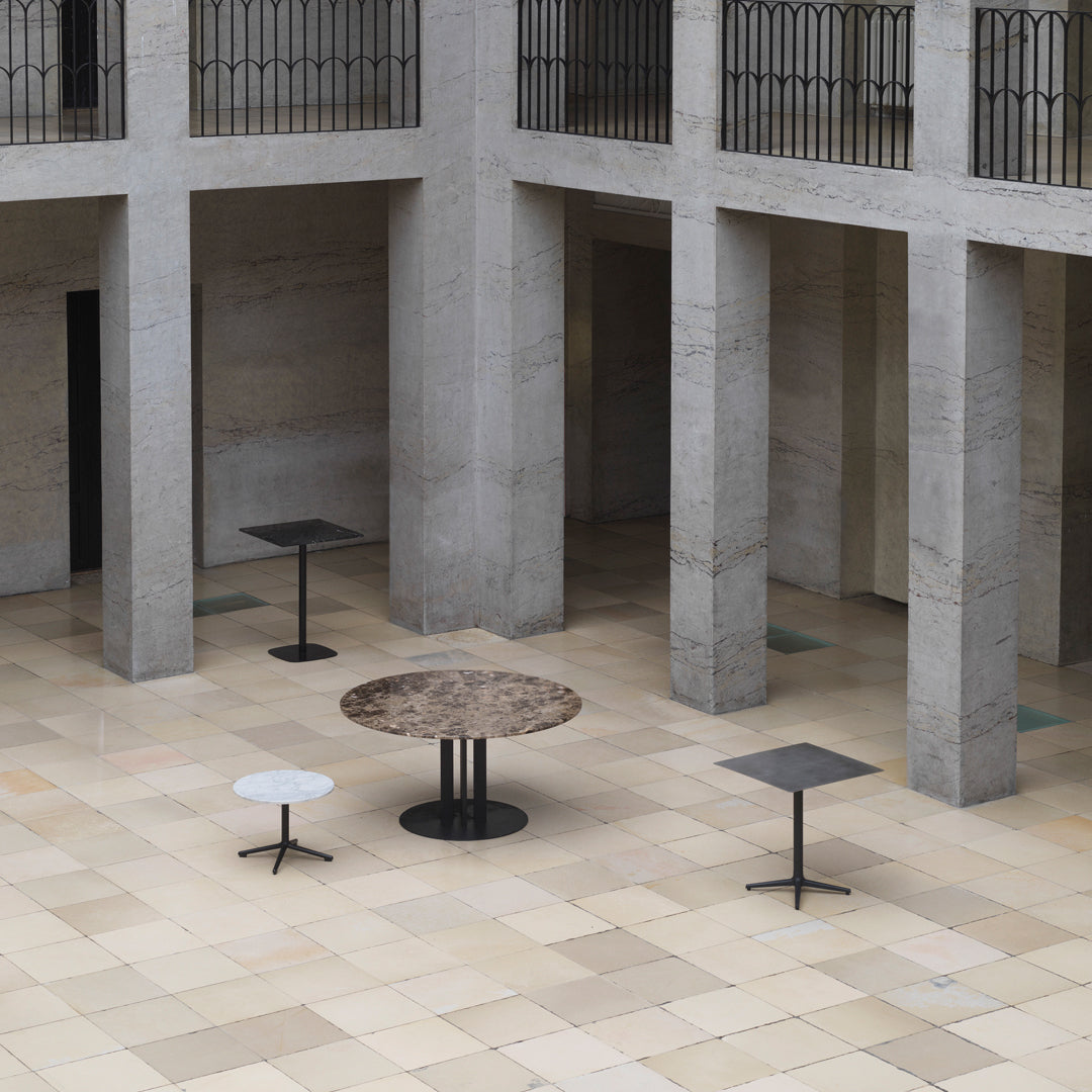 Modern tables featuring earthy tones, sleek black bases, and unique circular and rectangular patterns in an open space.