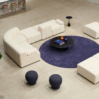 Curved cream sofa with purple circular rug, black round table, and navy stools in modern living space.