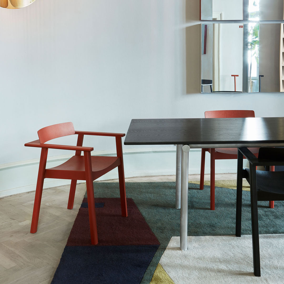 Red wooden chair against a multicolored area rug with blue, green, and yellow patterns and sleek black and silver table.