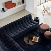 Modern navy blue tufted sofa with gray and rust accent pillows, complemented by round pink poufs and a circular black table.