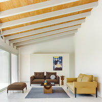 Modern living room featuring brown and mustard sofas, a geometric gray rug, and wooden beam ceiling accents.