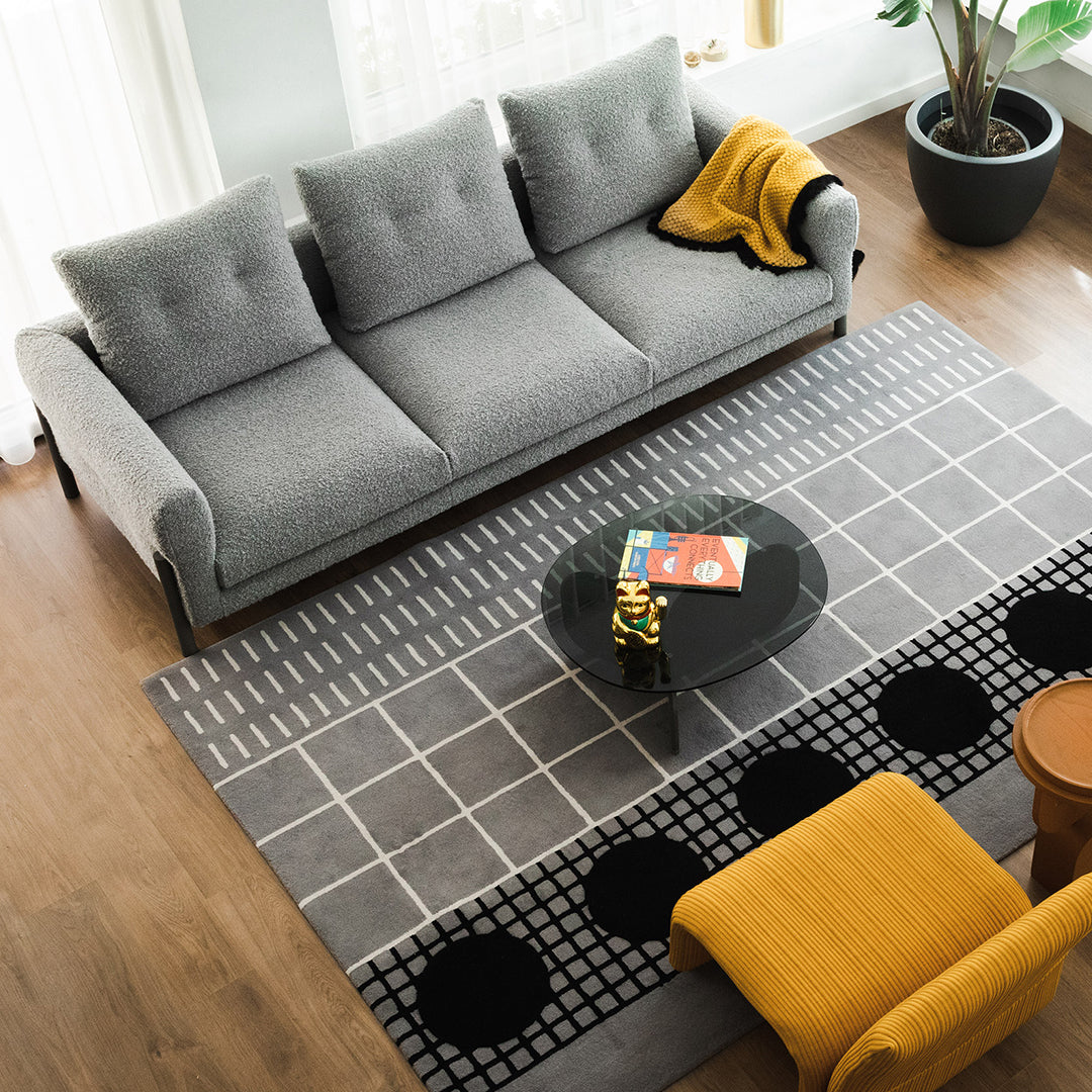 Gray sofa with light gray and black patterned rugs, accented by a yellow throw and modern black coffee table.