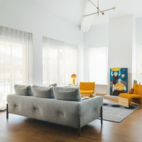 Gray tufted sofa, mustard yellow accent chairs, soft blue artwork, and geometric patterns on a light rug in a modern living room.