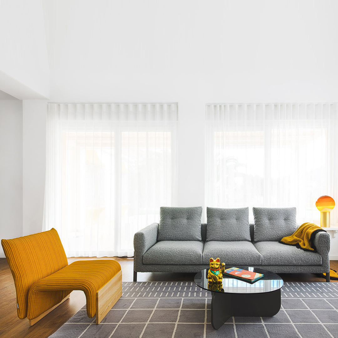 Grey sectional sofa with mustard yellow accent chair and geometric rug in a bright, minimalist living room setting.