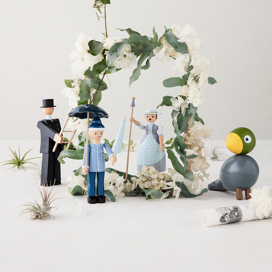 Colorful wooden figurines with blue, gray, black, and green accents surrounded by white floral decor and greenery.