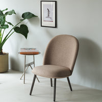 Beige upholstered chair with smooth, rounded design and black metal legs, set against a light grey wall.