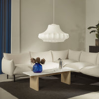 White scalloped pendant light above a beige sectional couch, with a blue vase and dark brown rug in a modern setting.