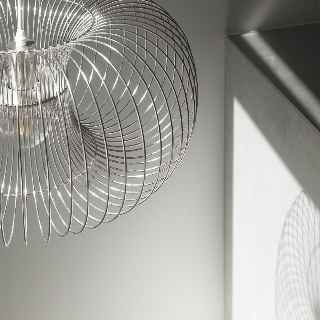 Silver wire pendant light casting intricate shadows on a gray wall, showcasing a modern, minimalist design.