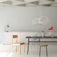 Modern minimalist dining room with light wood chair, black table, and transparent pendant lamp against a gray wall.