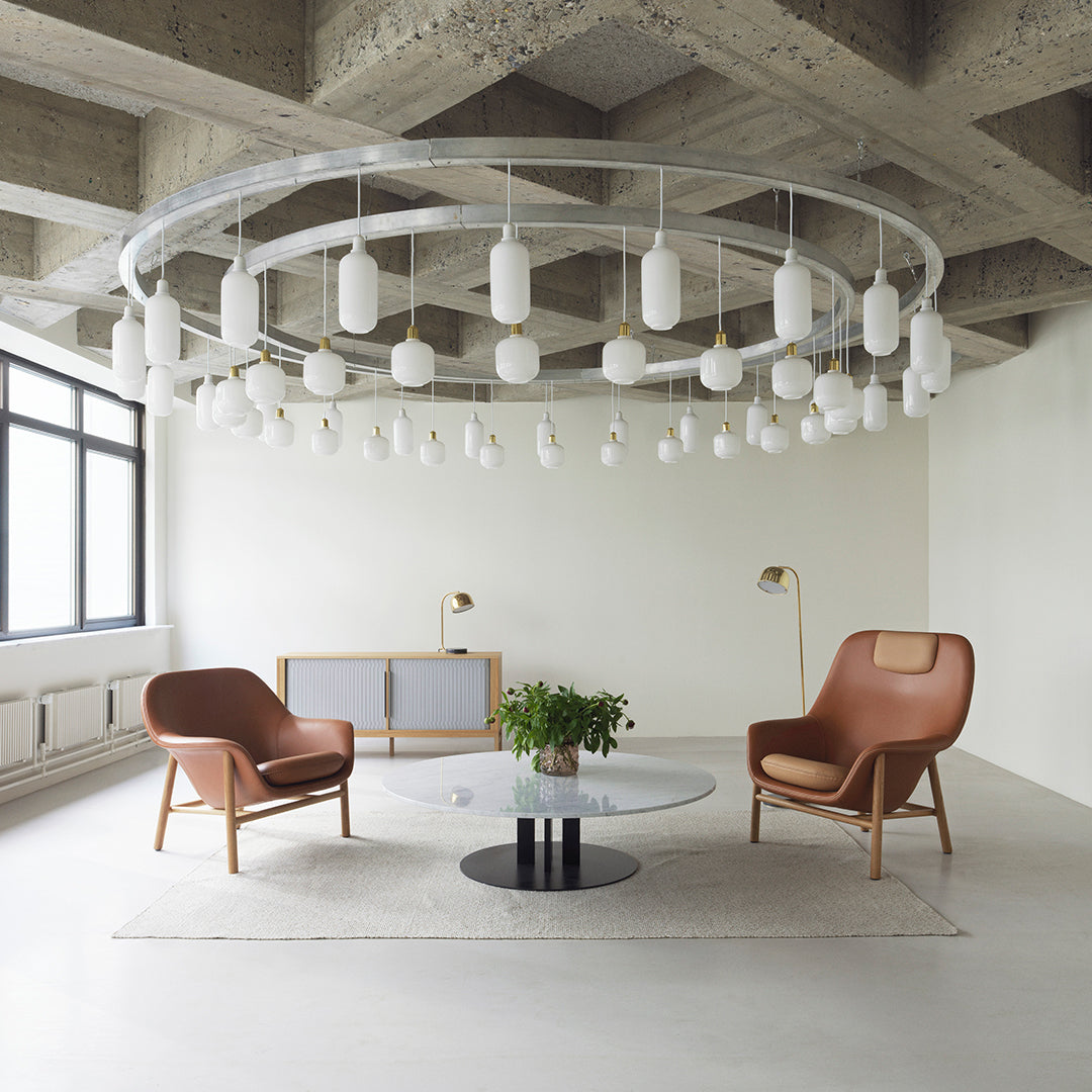 "Modern living room with brown leather chairs, a round black coffee table, and white pendant lights against a concrete ceiling."