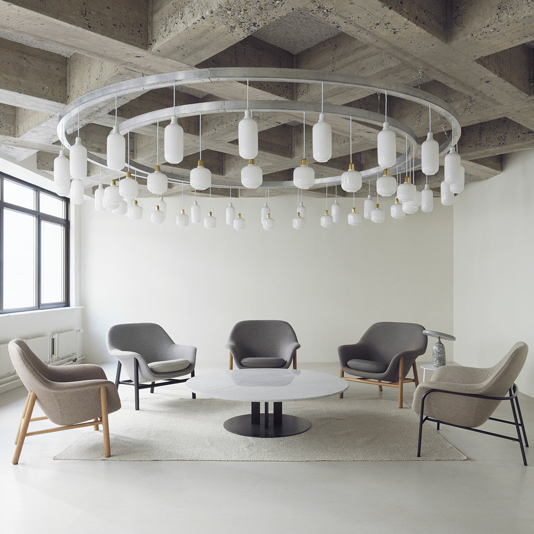 "Modern seating in shades of gray with light wood accents, featuring a minimalist round table and unique hanging lights."