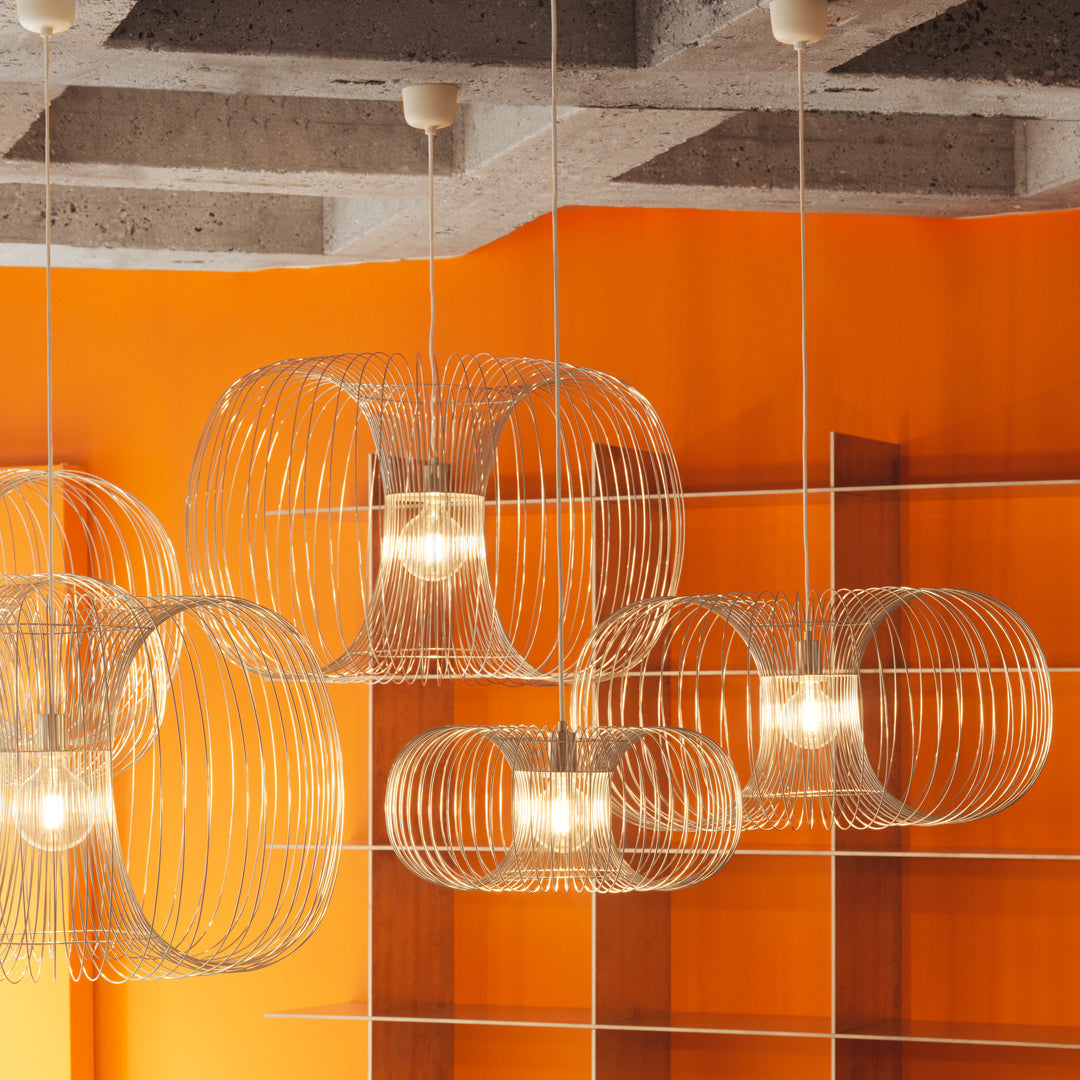 Transparent wire lamps with circular patterns against a vibrant orange wall and concrete ceiling.