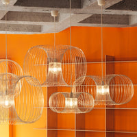Transparent wire lamps with circular patterns against a vibrant orange wall and concrete ceiling.