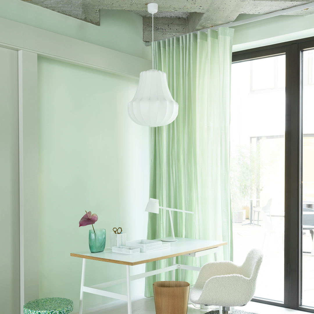Mint green walls and sheer green curtains complement a minimalist white desk and light fixtures. 