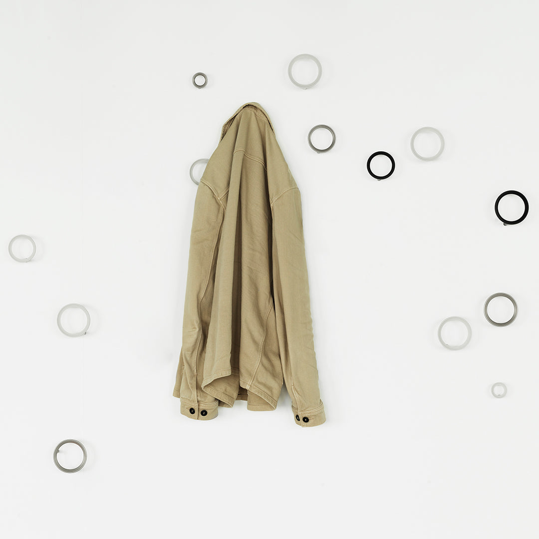 Light beige shirt hanging against a white wall, surrounded by circular gray and black wall decor.
