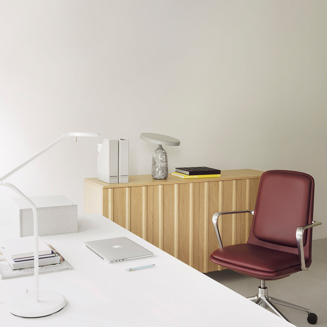 Modern office setting featuring a burgundy chair and light wood storage unit against a neutral wall, enhancing contemporary decor.